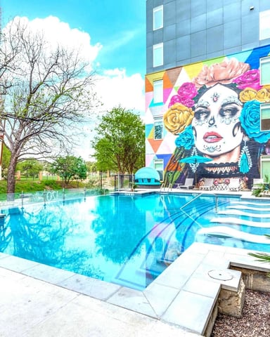 Resort pool with turquoise water and colorful geometric mural of a woman's face on building behind it