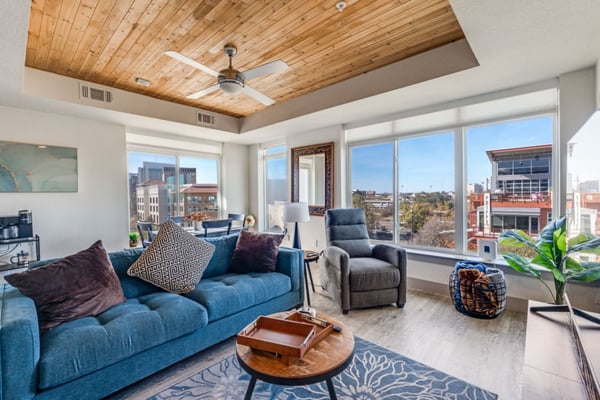 High-rise living room with blue sofa, wooden ceiling, floor-to-ceiling windows, and cityscape views