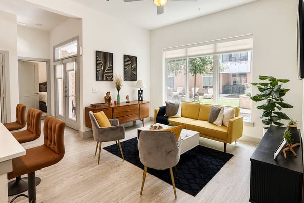 Modern living room with yellow sofa, gray armchairs, wood dresser, and sliding glass doors opening to patio